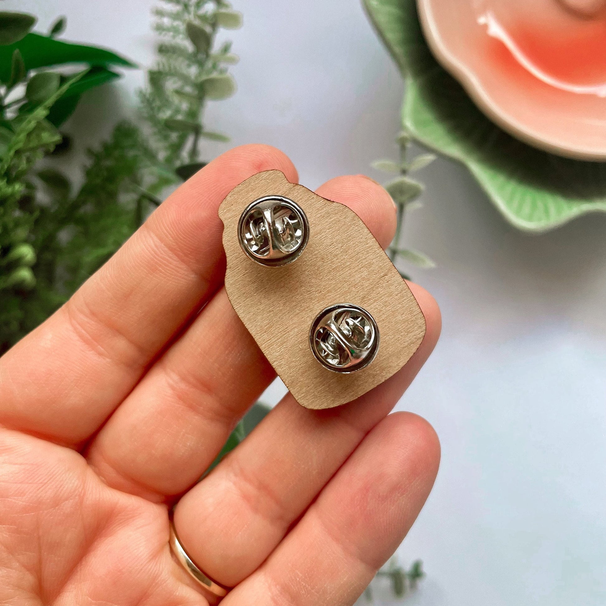 An eco friendly wooden pin badge, of a terrarium with greenery and toadstools inside. The pin badge has two back fastenings.