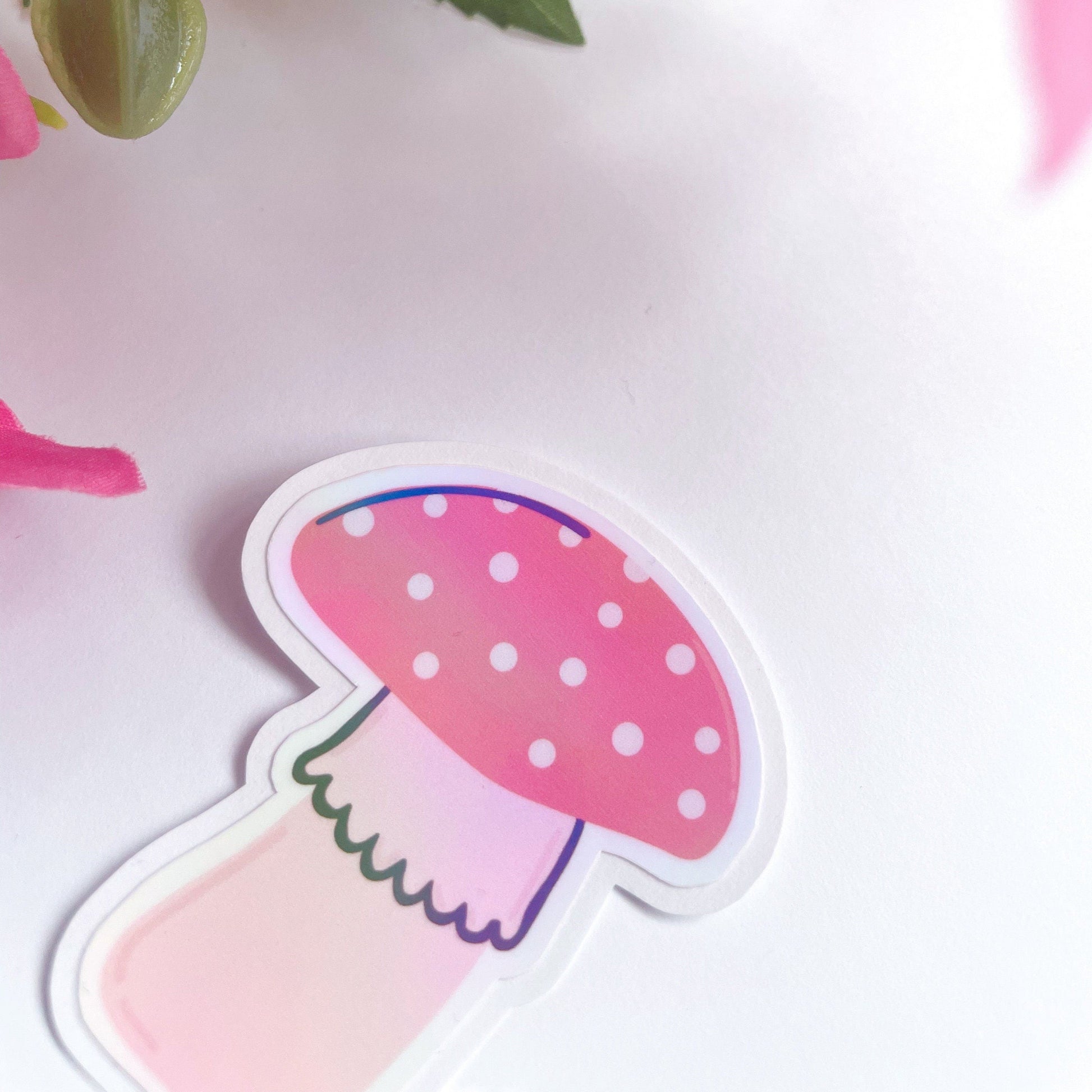 A holographic sticker, of two cute red and pink mushrooms. The sticker has an easy peel lip.