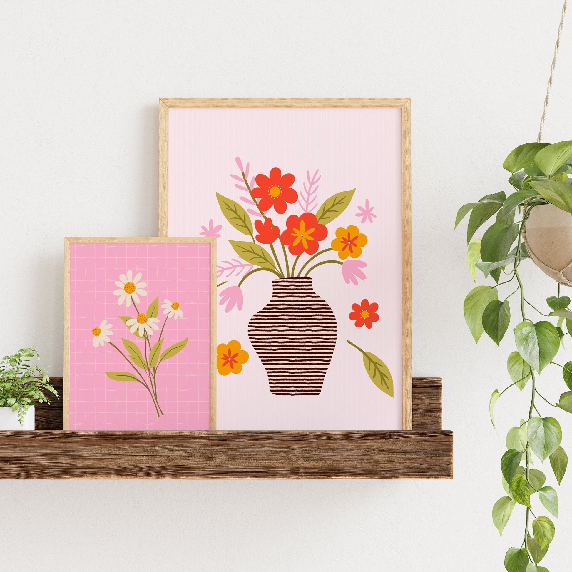 An illustration of aa vase of flowers, in shades of red, green and pink, shown in a frame, next to an illustration of  bunch of daisies on a pink background.