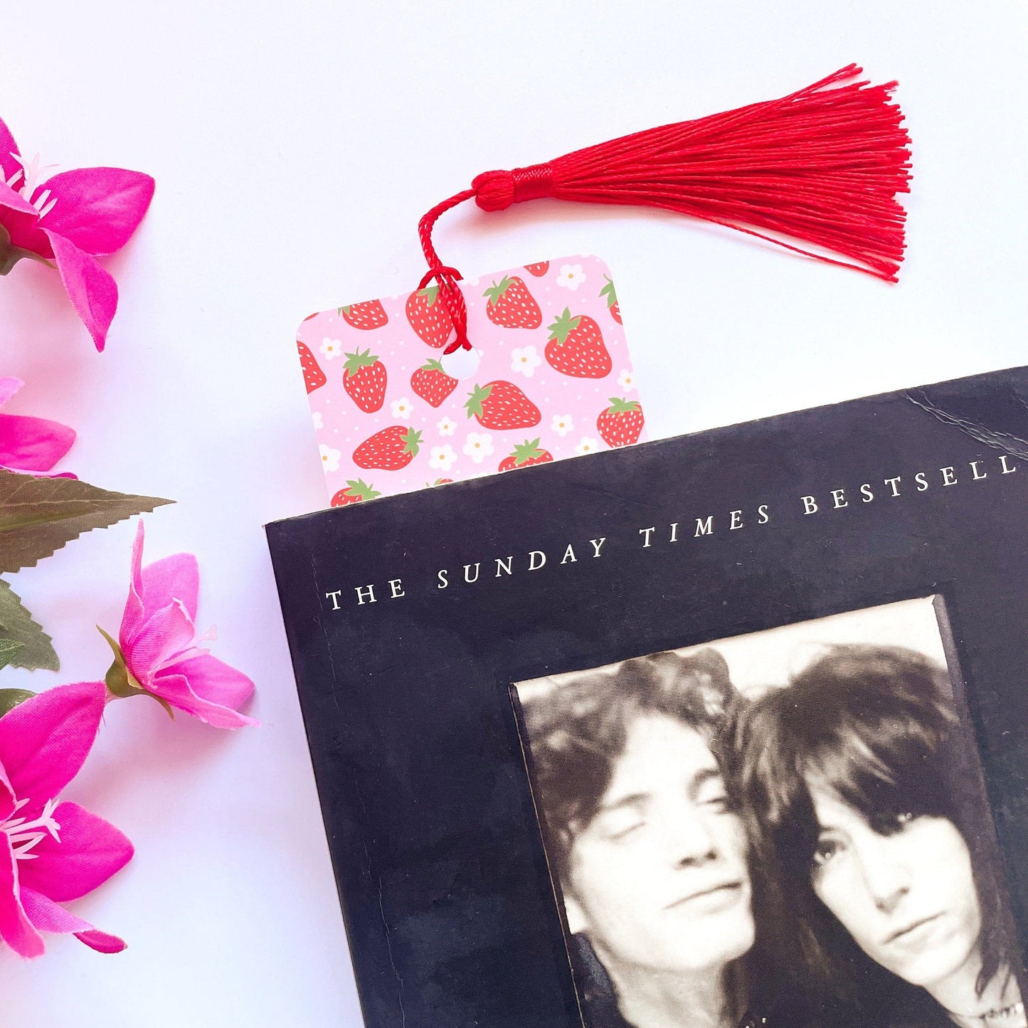 A picture of a pink and red bookmark, with a coordinating red tassel, with a cute strawberry print all over it.