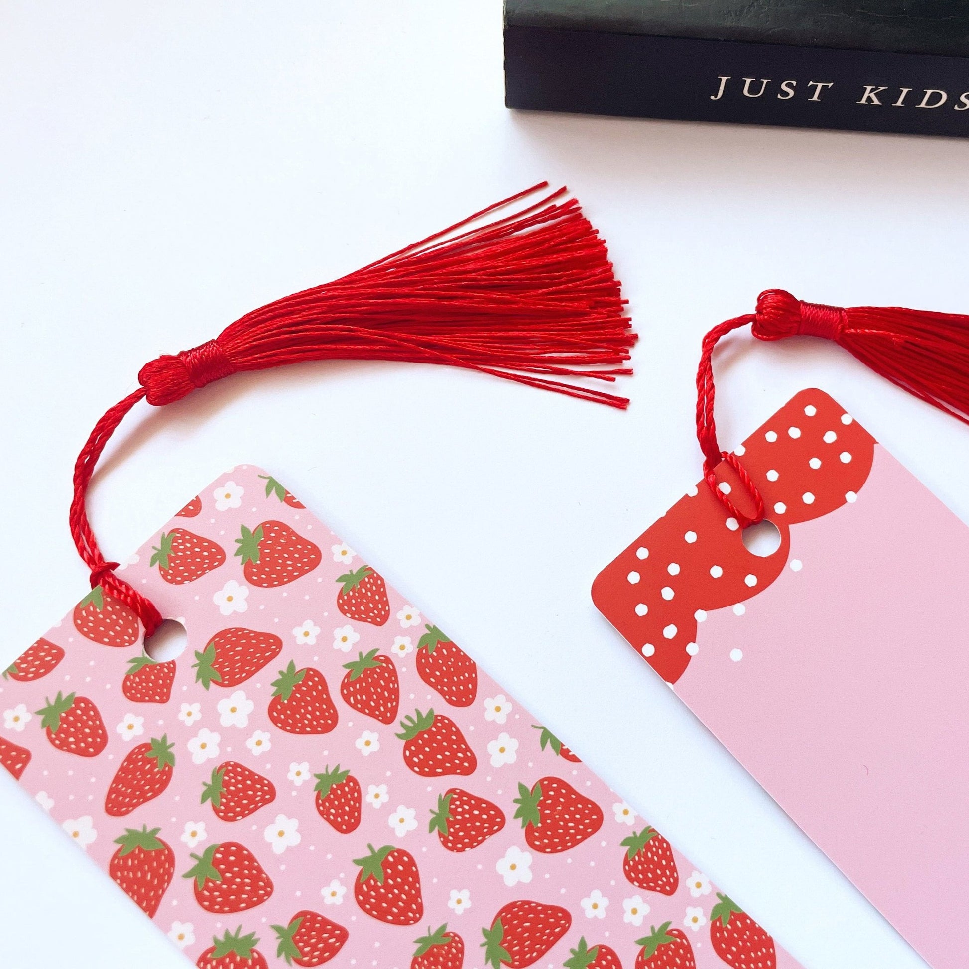 A picture of a pink and red bookmark, with a coordinating red tassel, with a cute strawberry print all over it.