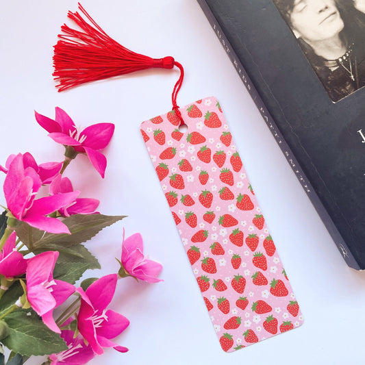 A picture of a pink and red bookmark, with a coordinating red tassel, with a cute strawberry print all over it.