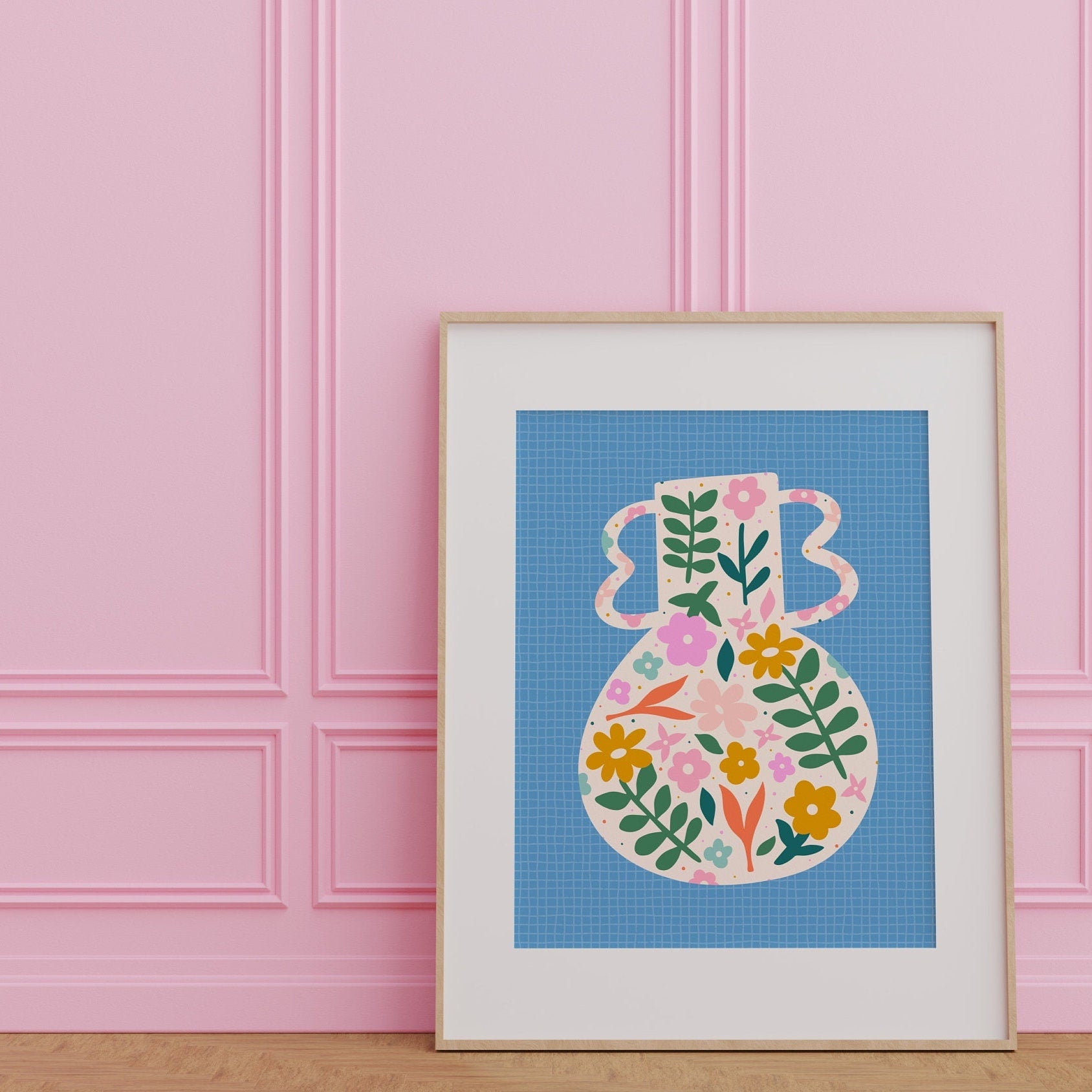A blue art print featuring a vibrant vase illustration with floral patterns against a blue textured background, presented against a white wall.